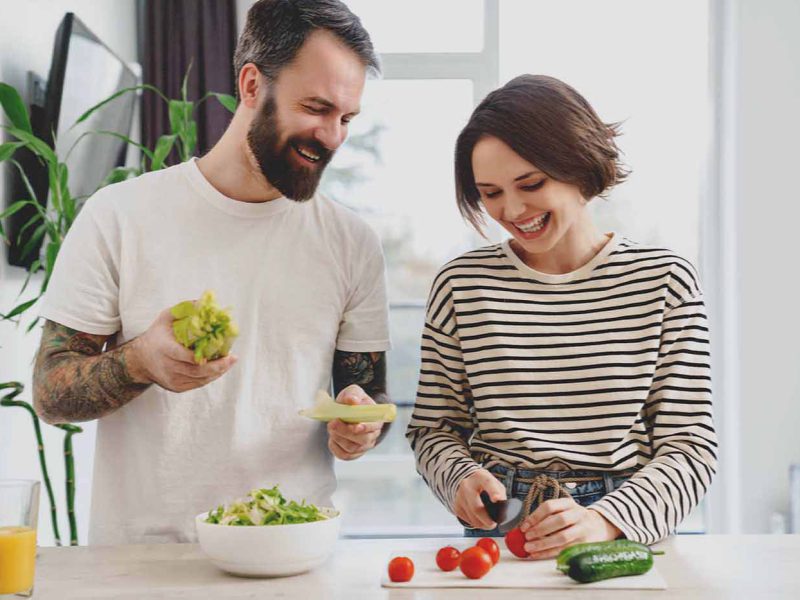 Young happy white couple cooking salad together